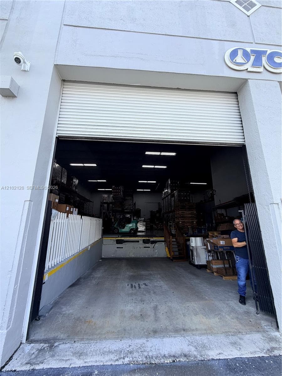 Roll-up door entry with concrete loading area, interior fluorescent lighting, and a security camera