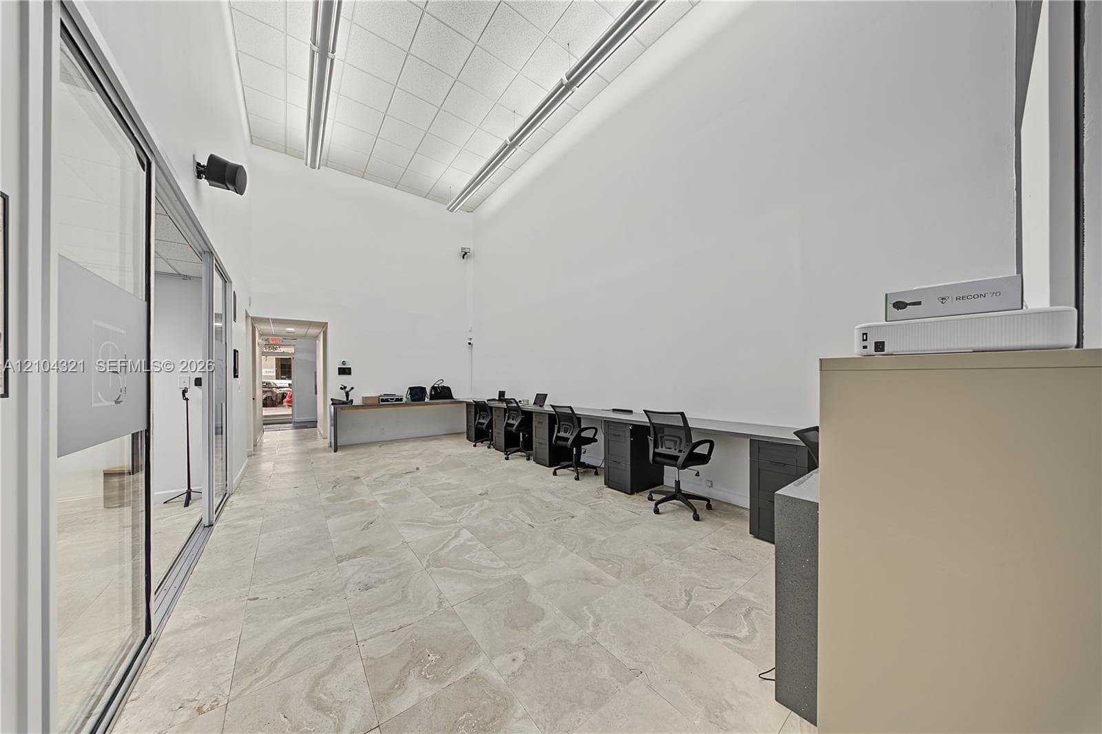 Open-concept interior featuring high ceilings, stone tile flooring, linear recessed lighting, and built-in cabinetry with a desk surface