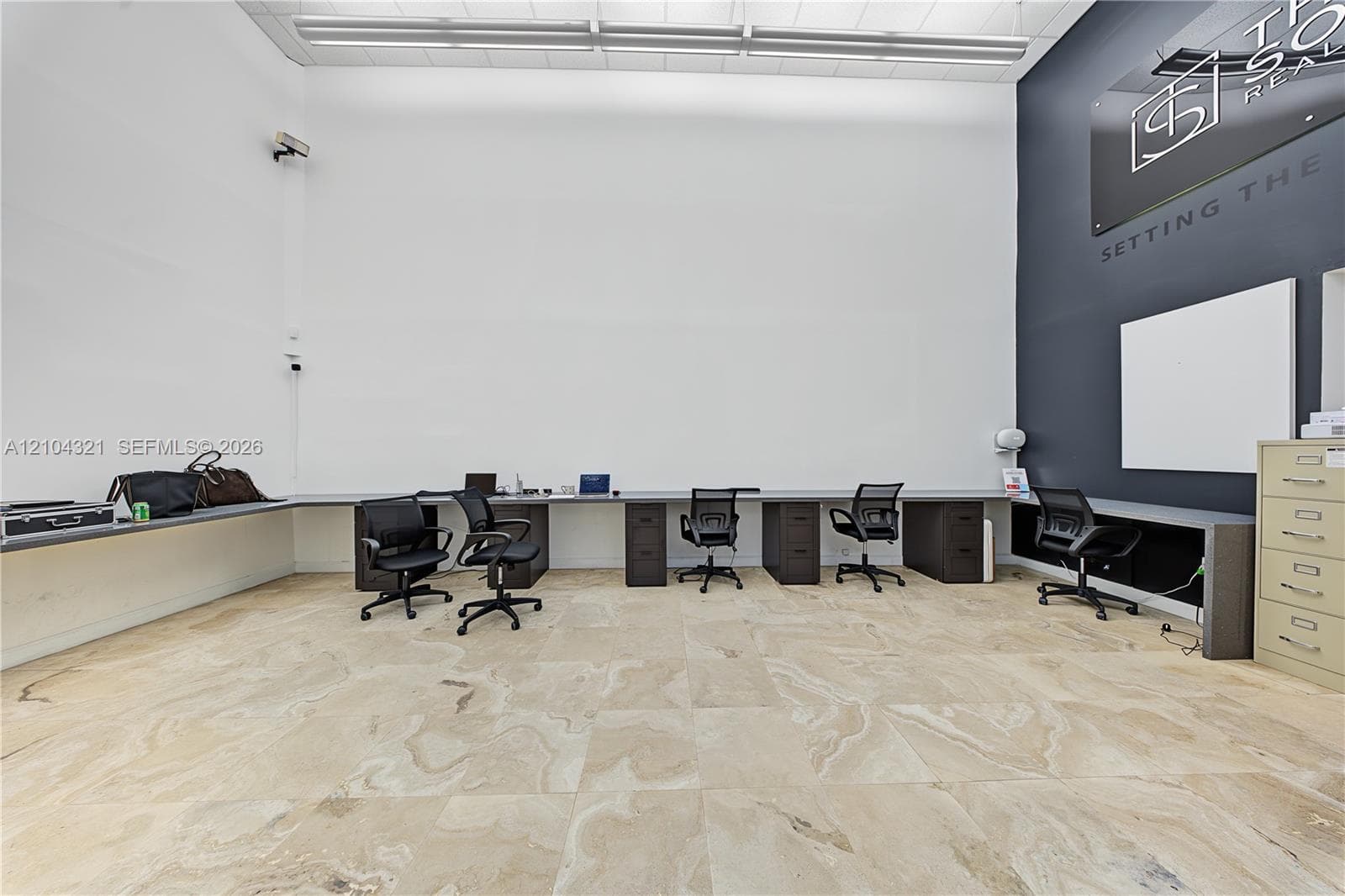 High-ceilinged room featuring neutral large-format tile flooring, integrated perimeter desk cabinetry, and a charcoal accent wall