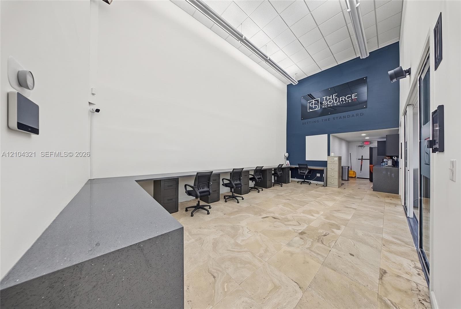High ceilings with recessed linear lighting, stone-finish tile flooring, built-in dual-tier desk station with quartz-style countertops, and accent wall