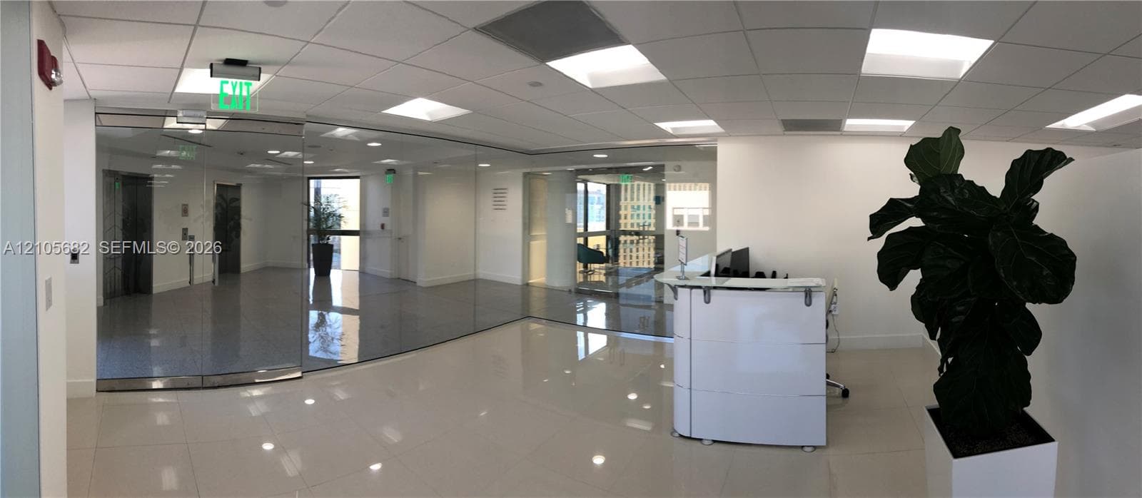 Reception area featuring large-format polished tile flooring, recessed grid ceiling with integrated panel lighting, floor-to-ceiling glass partitions, and a built-in modular reception desk