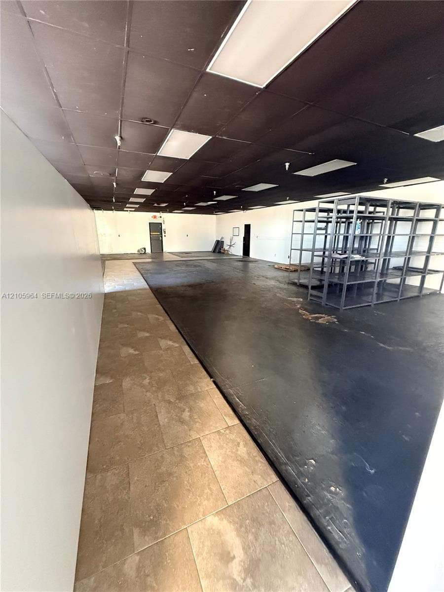 Open floor plan featuring a combination of tile flooring and dark-finished concrete flooring, dark drop ceiling with recessed lighting, and built-in metal shelving units