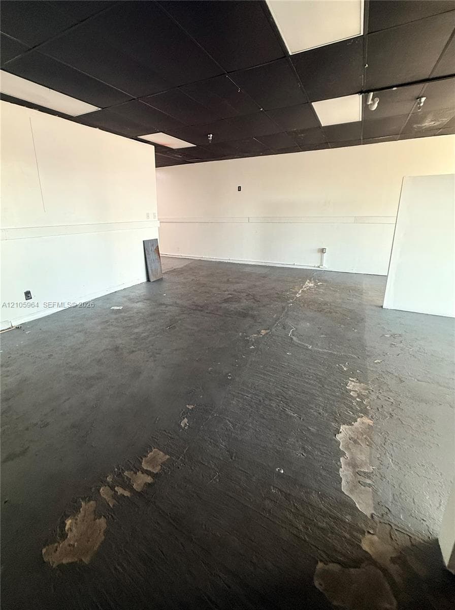 Open-concept interior featuring painted walls, a dark-toned drop ceiling with inset lighting, and exposed concrete flooring