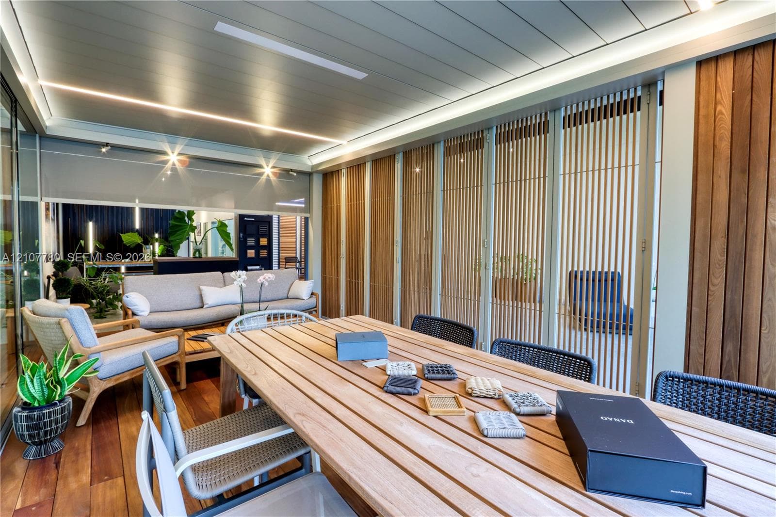 Covered outdoor living space featuring wood-finish flooring, a paneled ceiling with integrated linear LED lighting, and vertical slatted wood screen walls