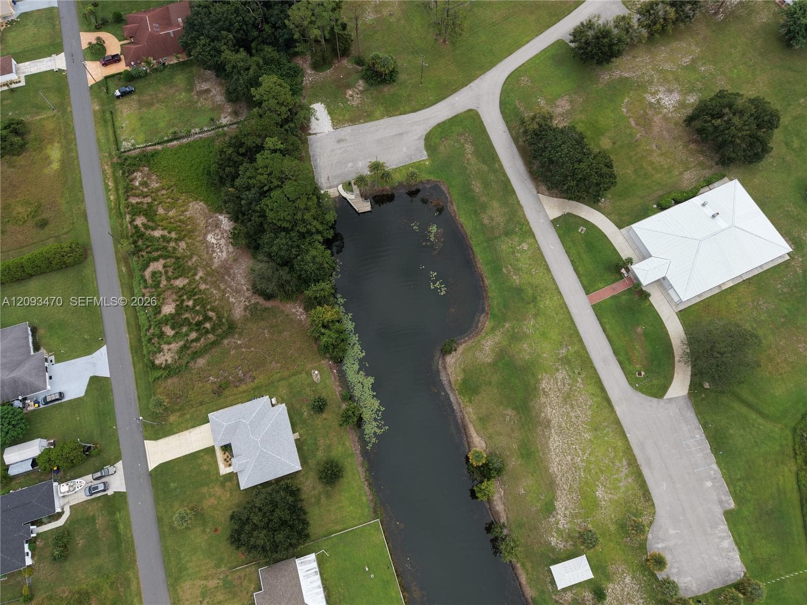 Aerial perspective of expansive grounds featuring a private pond, paved driveway, mature trees, and open grass landscape
