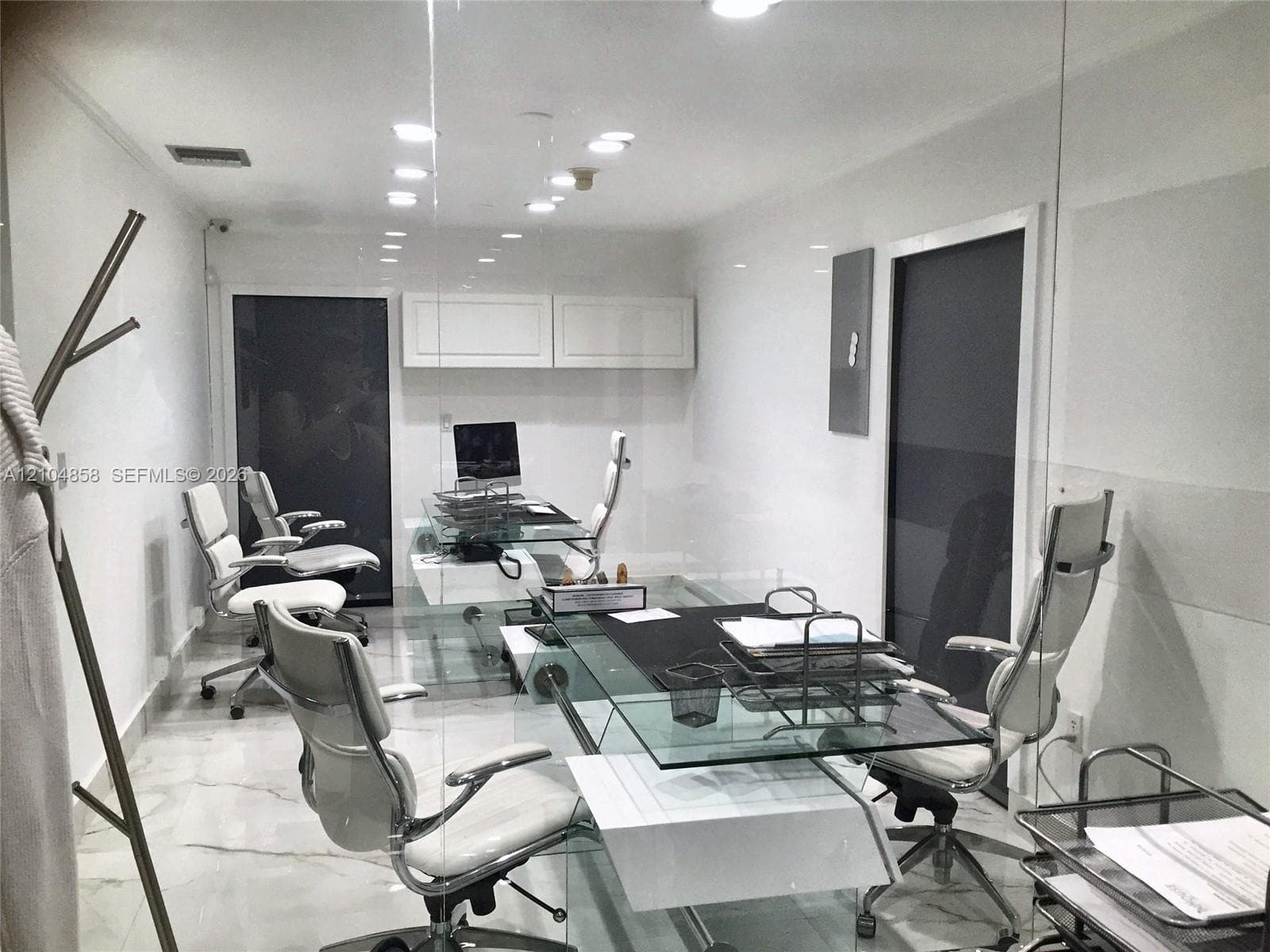 Polished stone flooring, recessed ceiling lighting, wall-mounted upper cabinetry, and glass-partitioned wall enclosure
