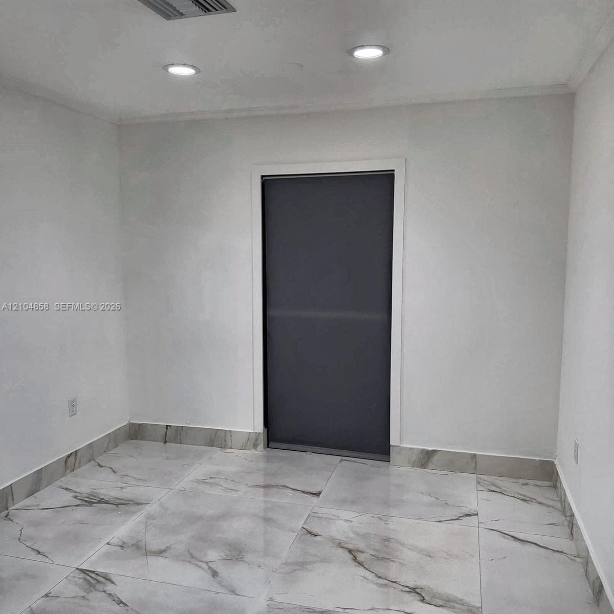 Large-format stone-look floor tiling with matching wall trim, recessed ceiling lighting, and a single-panel interior door