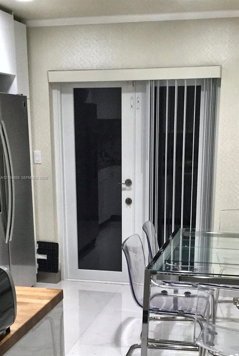 Full-light glass exterior door featuring a white frame and brushed metal hardware, complemented by white vertical blinds and neutral textured wall finishes