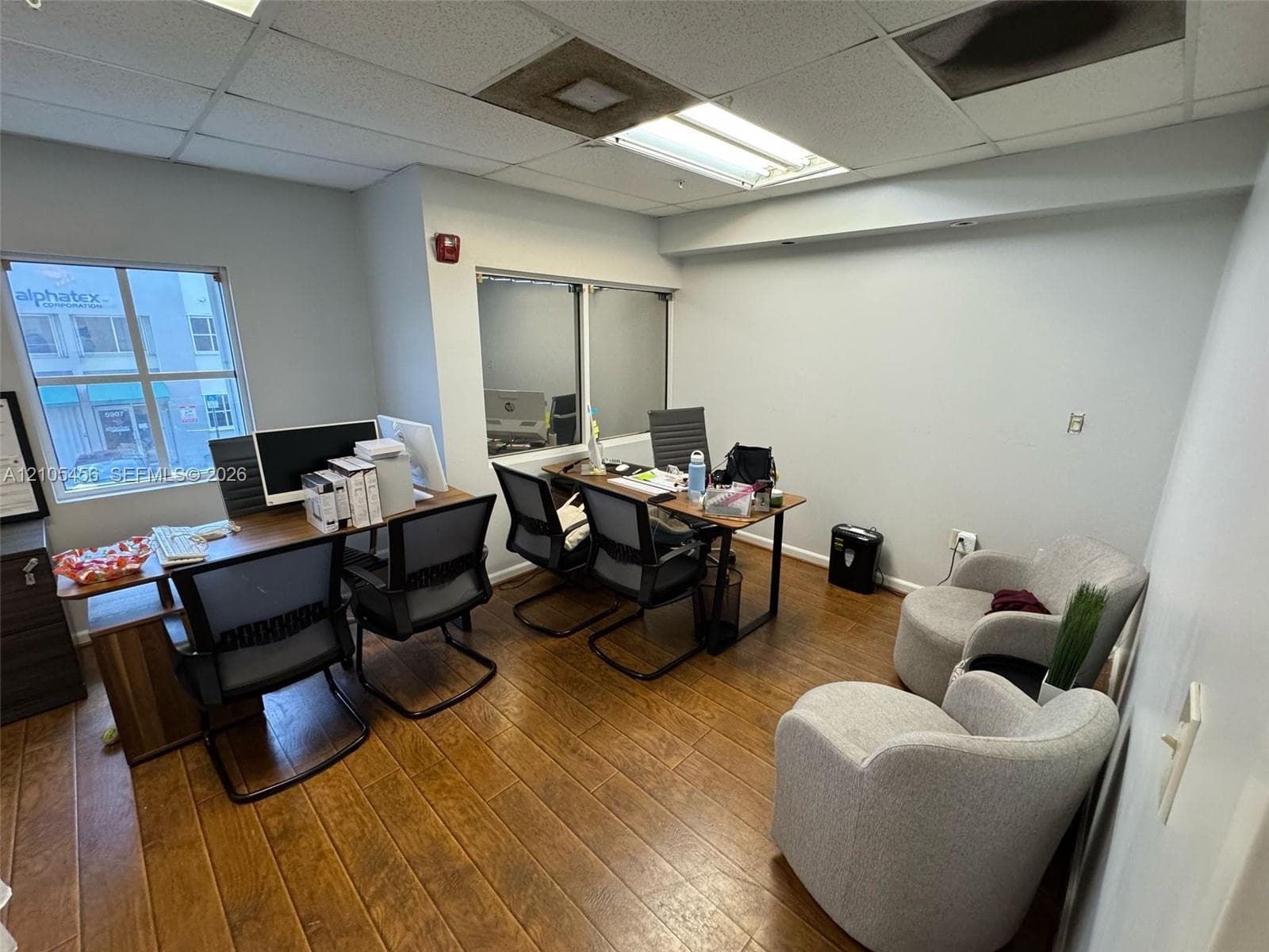 Office space featuring wood-finish flooring, dual windows with natural light, and drop ceiling with recessed lighting