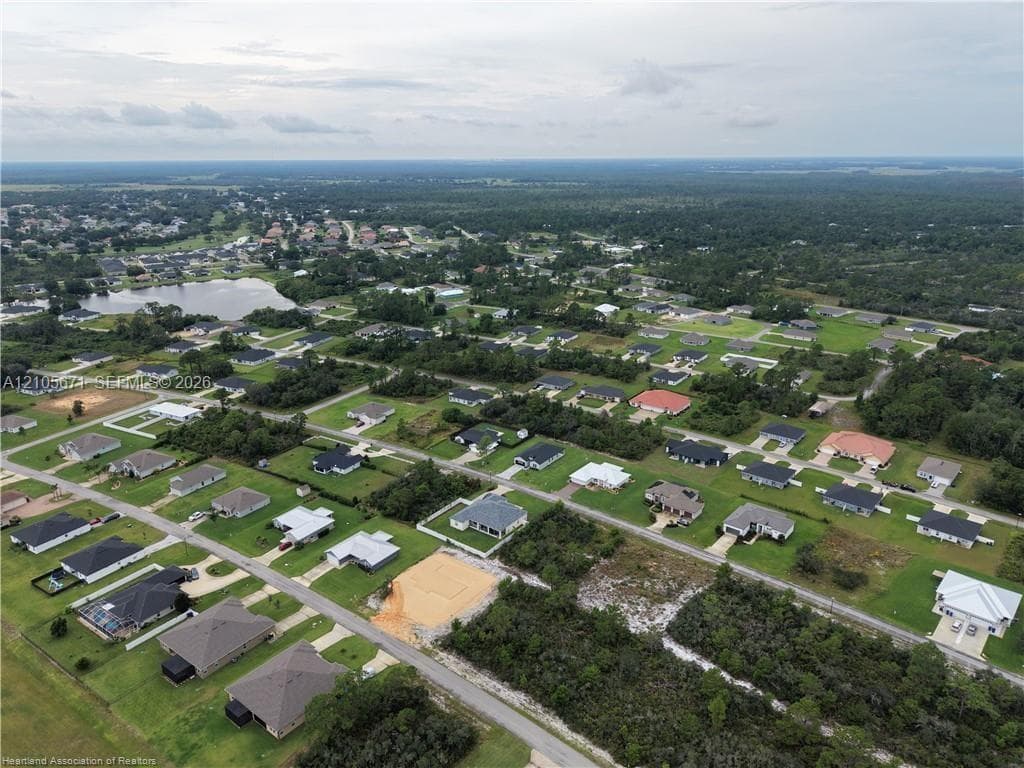 Aerial perspective of a residential development featuring paved street infrastructure, landscaped grass lots, and a water feature