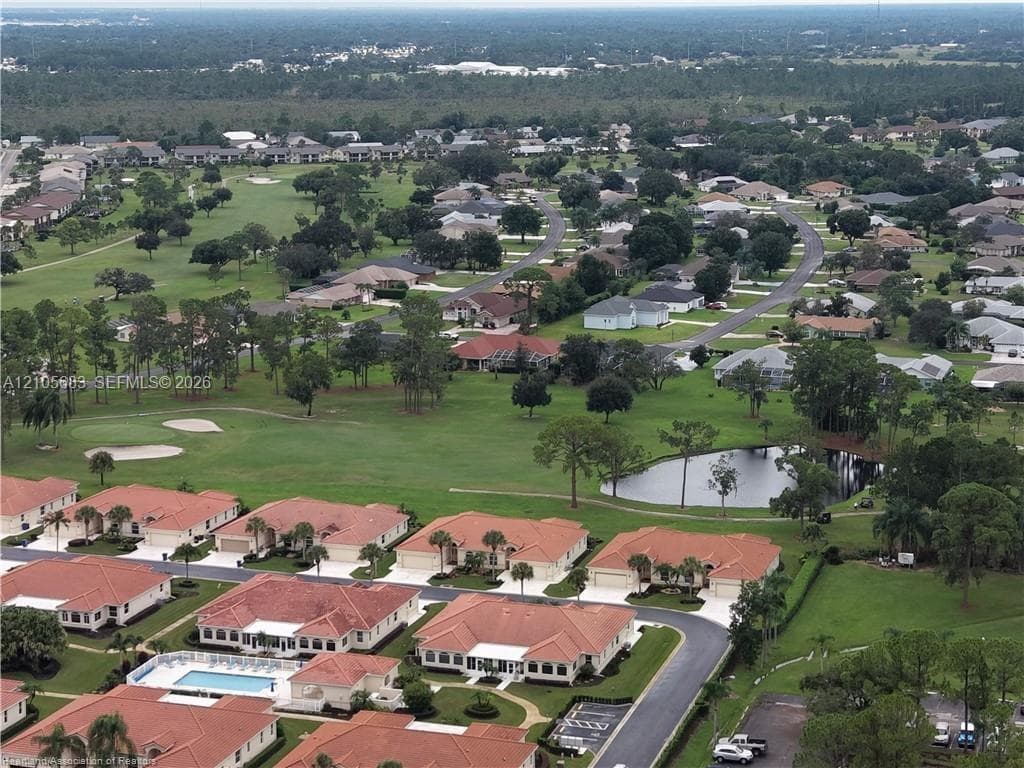 Aerial perspective featuring residential structures with clay tile roofing, manicured green space, a community swimming pool, and proximity to a golf course fairway and pond