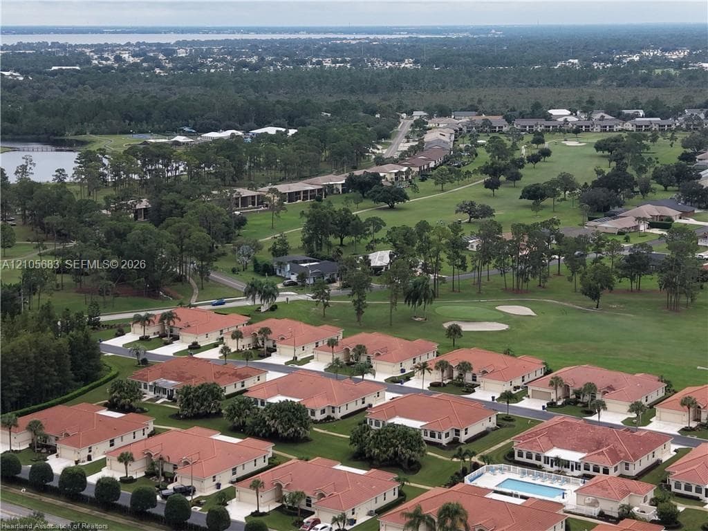 Aerial perspective of a community featuring terracotta-tiled roofs, manicured lawns, mature landscaping, paved roadways, and a communal pool