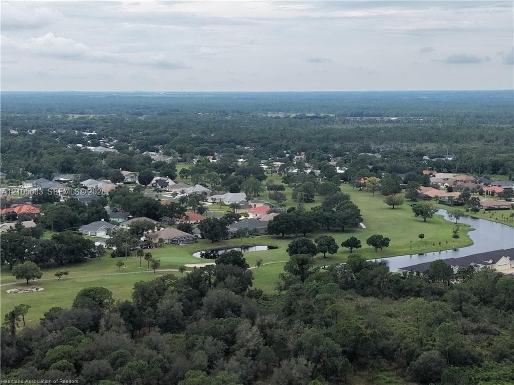 Aerial perspective of a sprawling landscape featuring expansive green terrain, mature tree groupings, and integrated water features