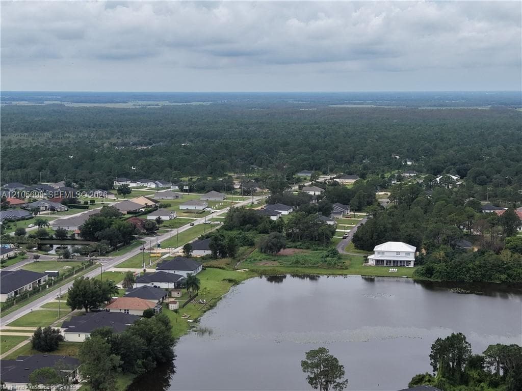 Aerial perspective featuring a two-story residence situated on a waterfront lot with expansive surrounding green space and mature trees