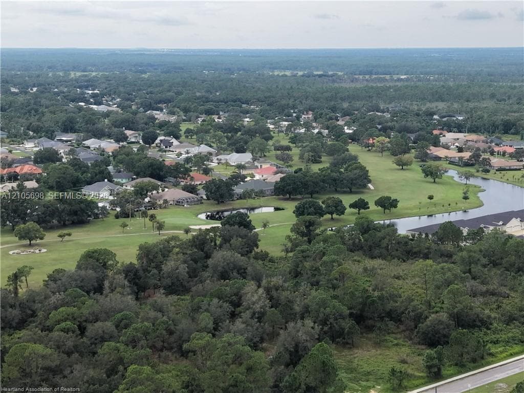 Aerial perspective of a sprawling residential area featuring expansive green space, mature trees, winding water features, and golf course fairways