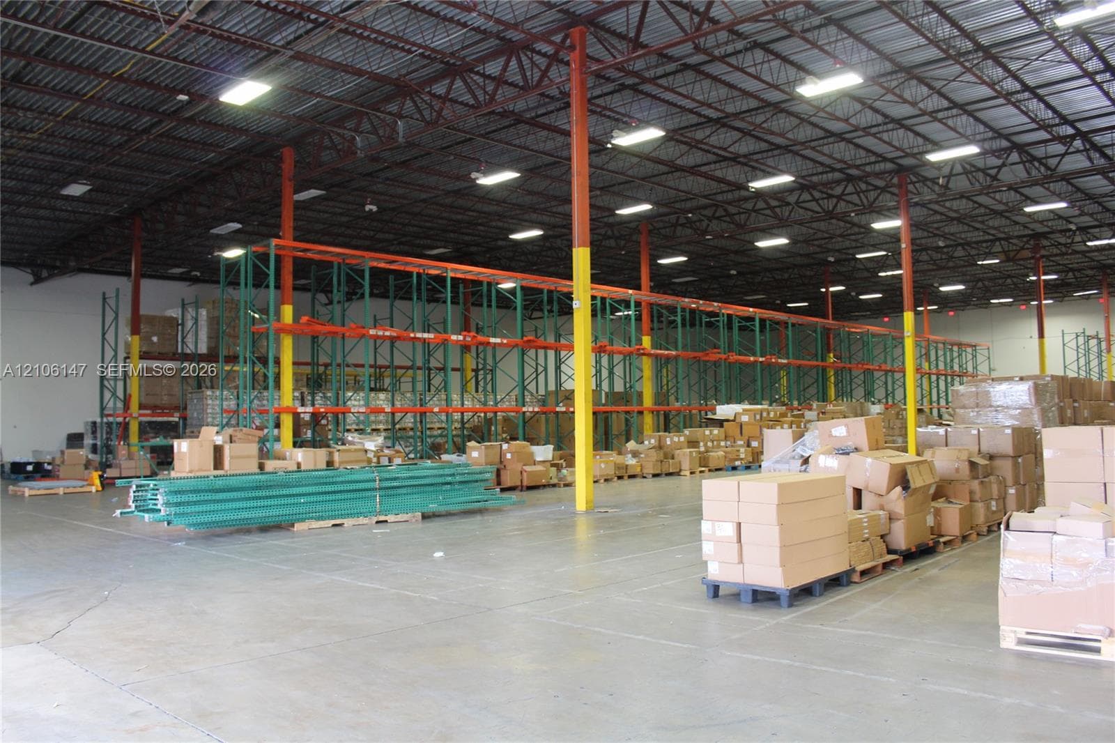 Warehouse interior featuring high-clearance open-span ceilings, steel truss construction, industrial lighting fixtures, concrete flooring, and installed pallet racking systems