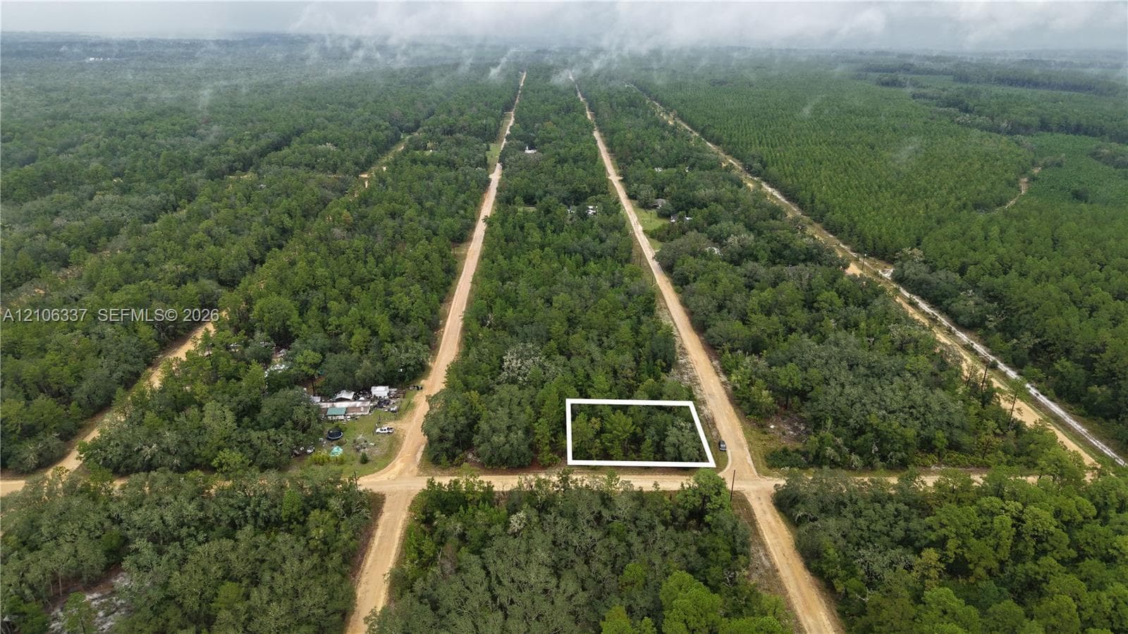 Aerial view of a vacant lot featuring dense tree cover and corner placement with dirt road frontage