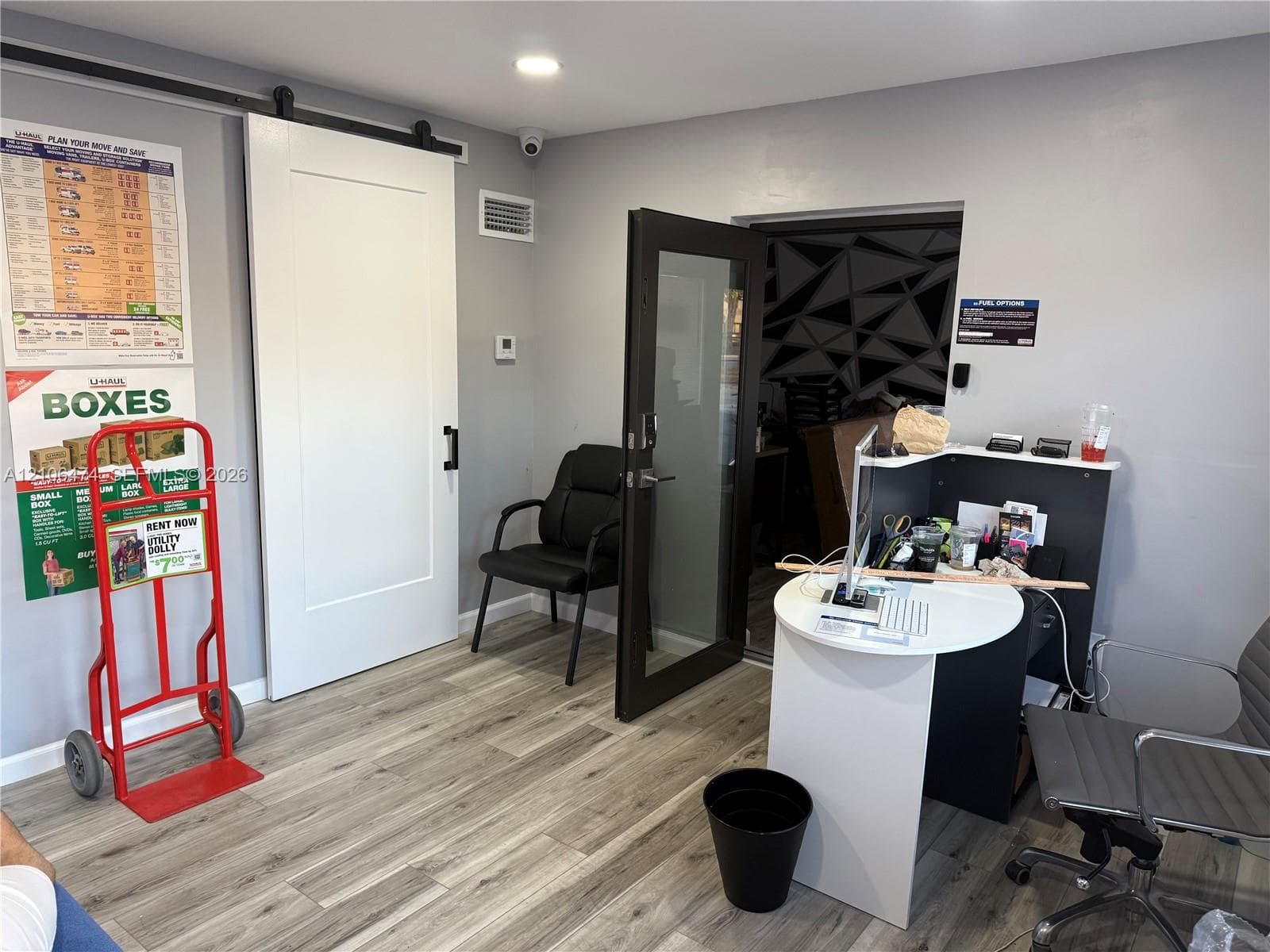 Interior space featuring wood-finish flooring, white shaker-style sliding barn door with black hardware, and a dark-framed glass panel door with integrated lock