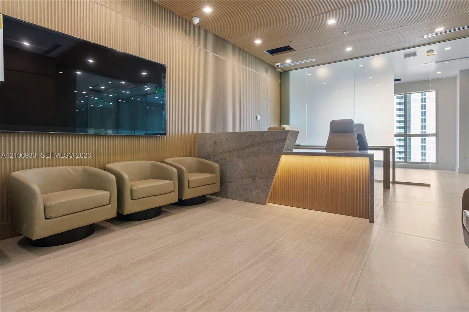 Reception area featuring ribbed wood wall paneling, a stone-faced built-in reception desk with integrated lighting, recessed ceiling lighting, and large-format tile flooring