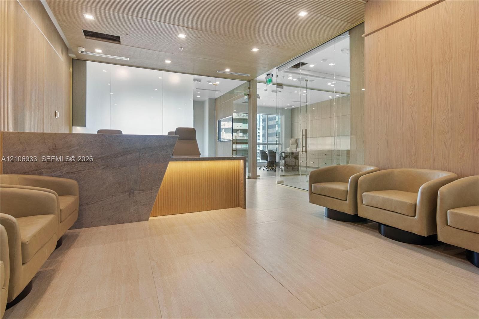 Reception area featuring wood-panelled walls, light-toned tile flooring, recessed ceiling lighting, and a geometric stone-surfaced desk with integrated under-counter lighting