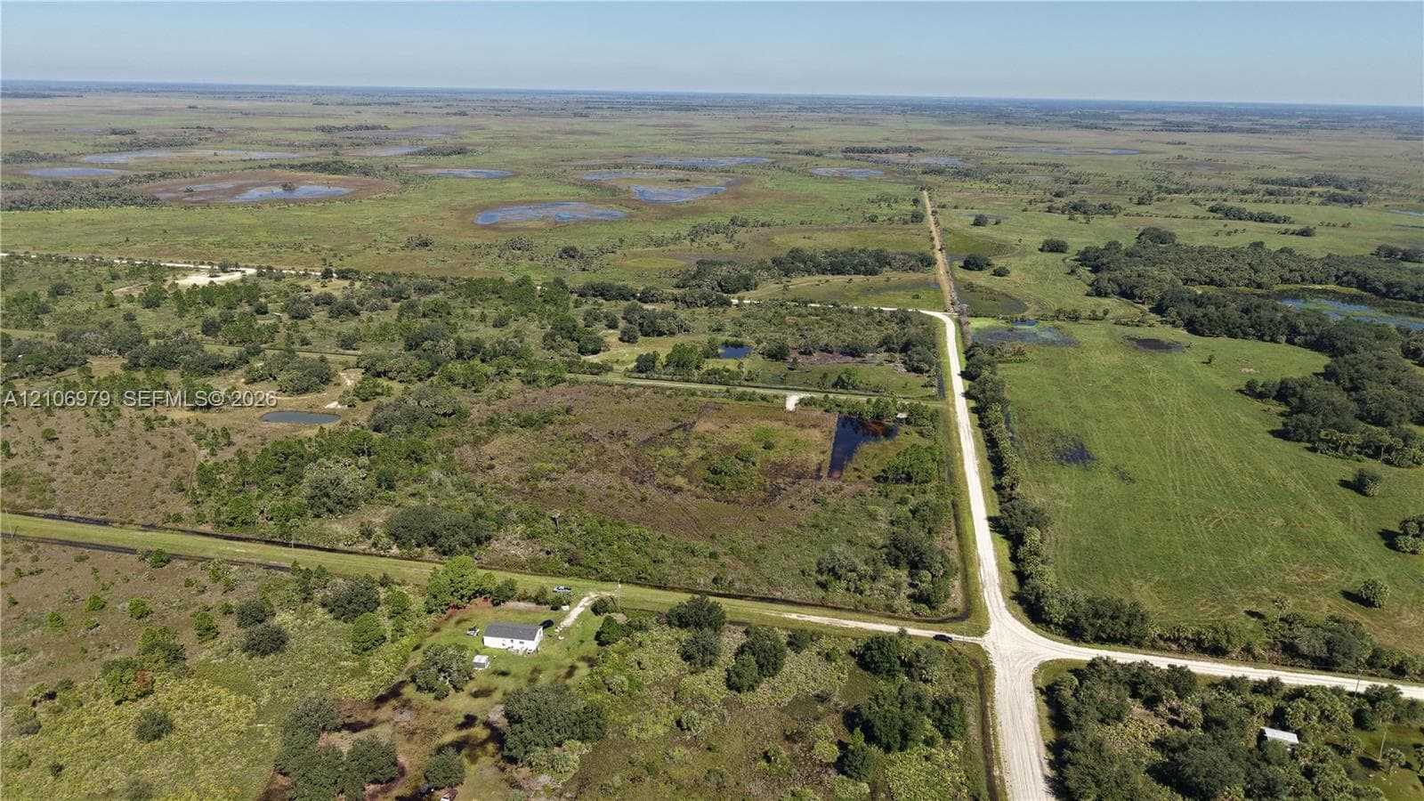 Expansive acreage featuring cleared pasture land, clusters of mature trees, natural water features, and frontage on an unpaved road