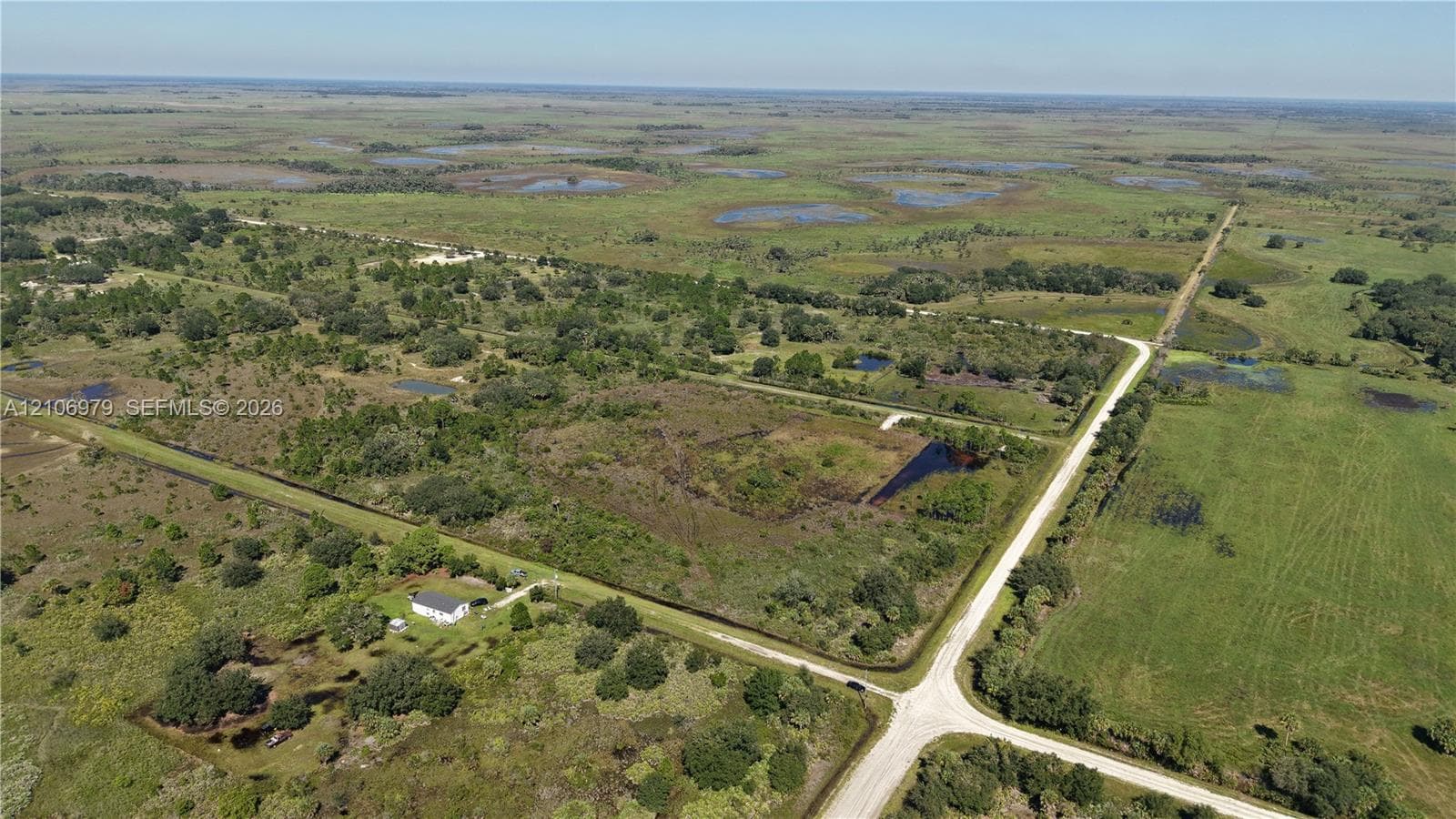 Expansive acreage featuring cleared land, clusters of mature trees, multiple water features, and paved road access