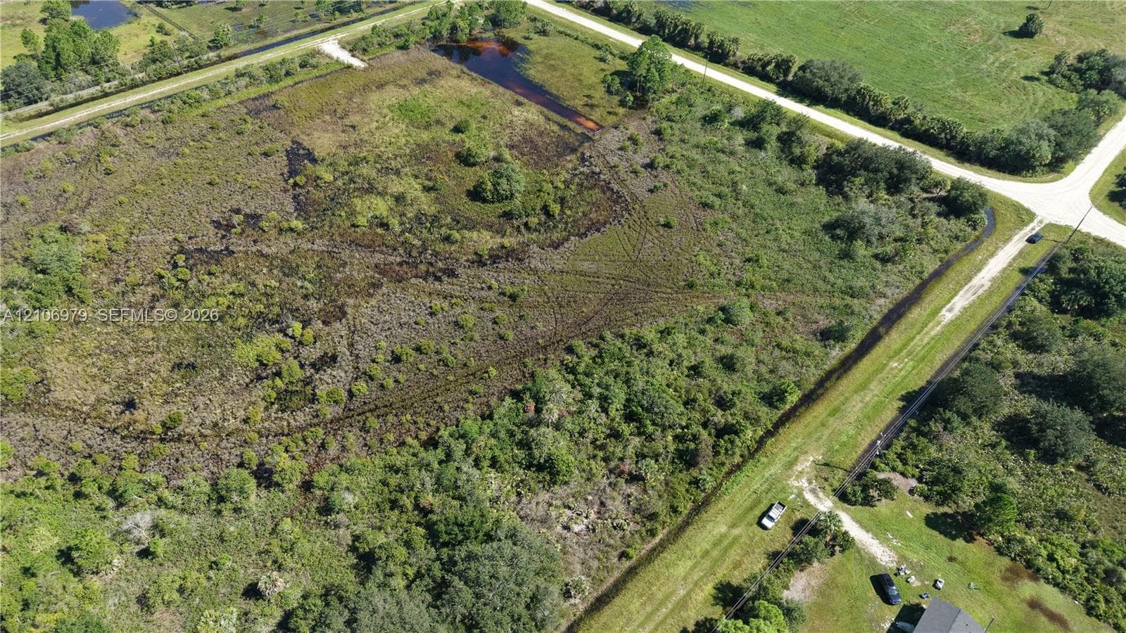 Expansive undeveloped acreage featuring native vegetation, established tree clusters, natural wetlands, and corner-lot positioning with paved road access